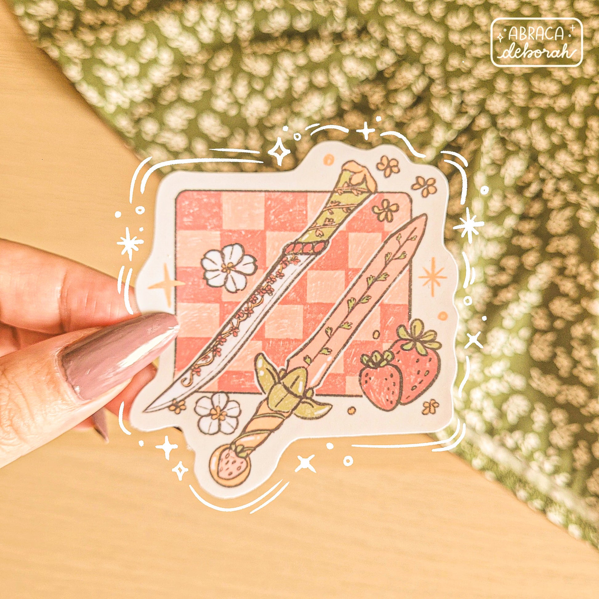 Stickers of two decorated swords, strawberries and flowers on a pink checked background.
