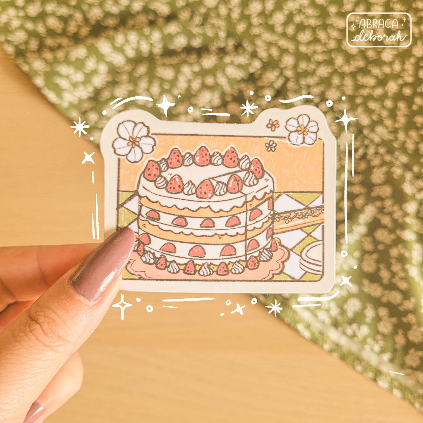 Sticker of a strawberry shortcake on a checked tablecloth. A slice is being cut out of the cake.