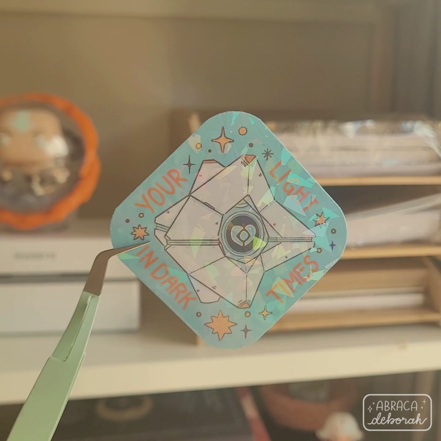 Holographic sticker of a diamond shaped machine with a light core in the middle. The words "Your light in dark times" are around the design.