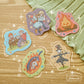 Five colourful stickers depicting different characters including a fire, a scarecrow, a couple, and an elderly woman with a child.