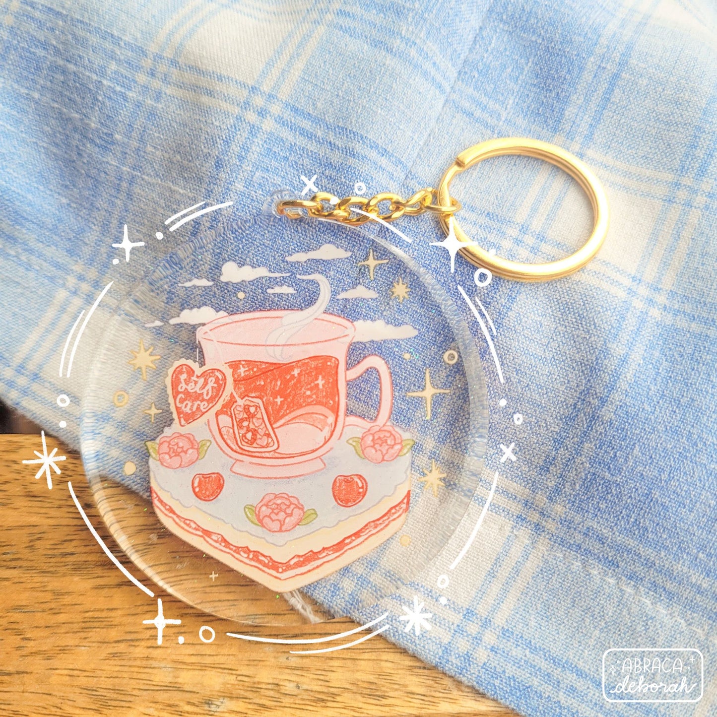 Round acrylic keyring with an illustration of a cup of tea sitting on a slice of cake. The teabag label says "Self Care".