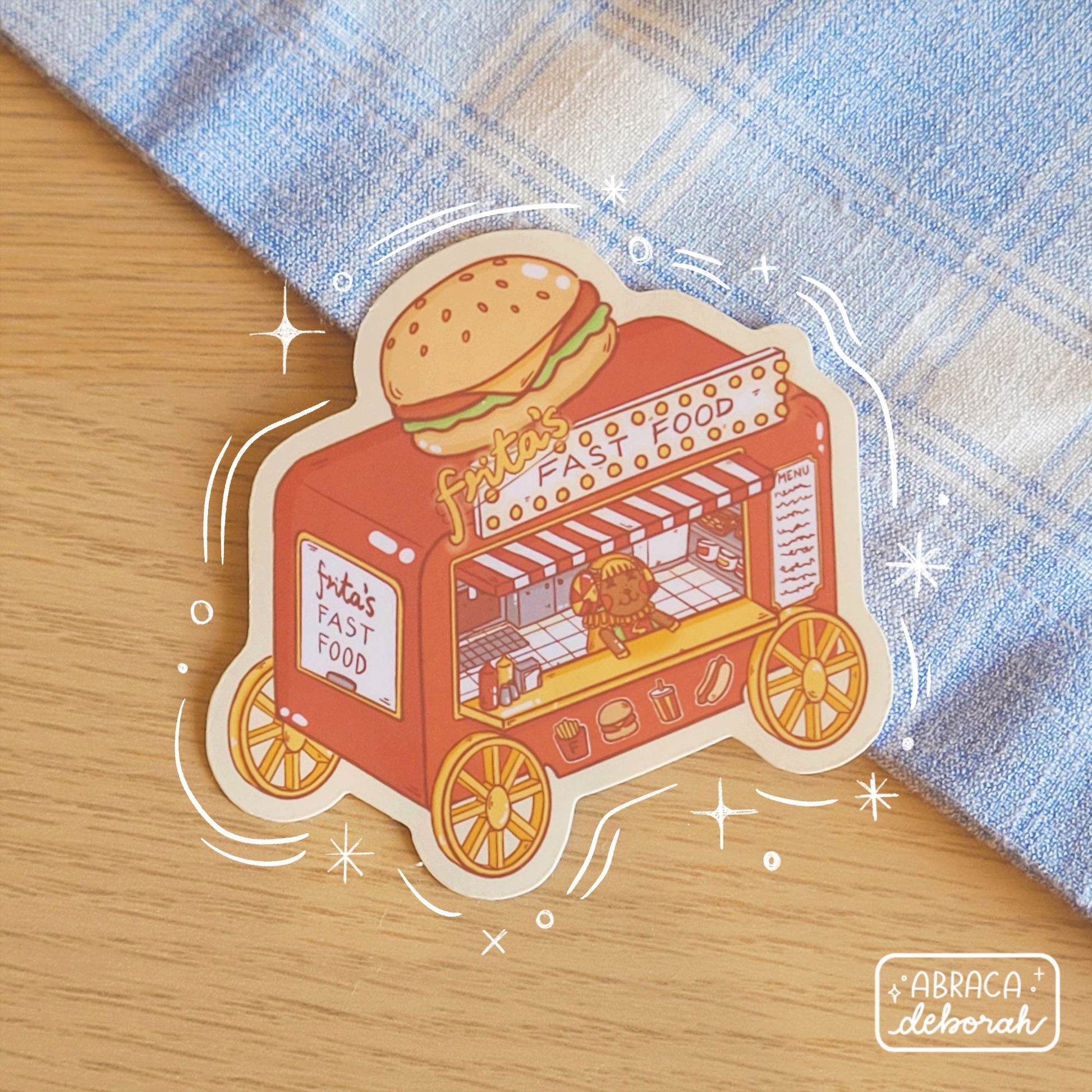 A sticker depicting a fast food truck with a large burger on top of it. A sheep stands inside it.