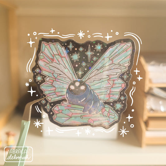 Holographic sticker of a luminous moth with three eyes, featherlike antennae and wings made of iridescent crystals.