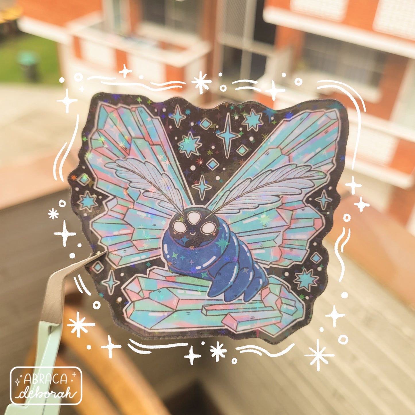 Holographic sticker of a luminous moth with three eyes, featherlike antennae and wings made of iridescent crystals.