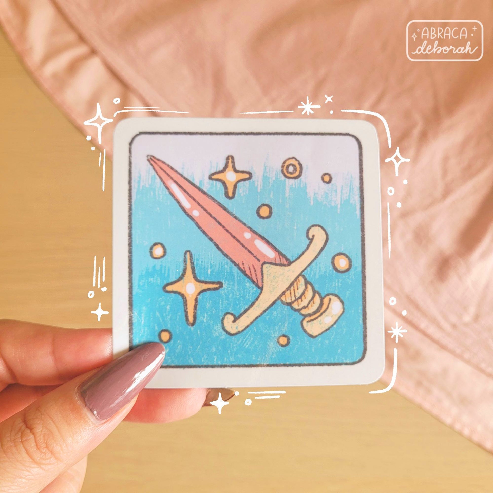 A square sticker depicting a pink sword with a golden coloured handle.