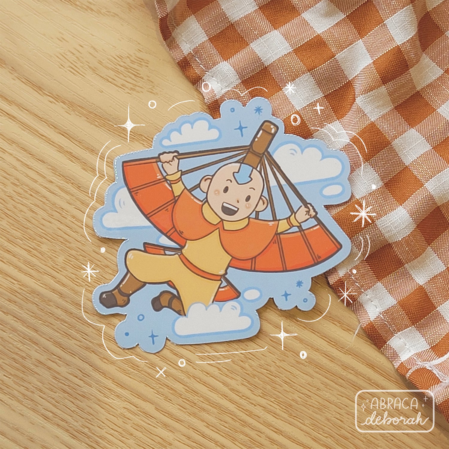 Sticker of an orange clad boy using a glider to fly. He has an arrow on his forehead.